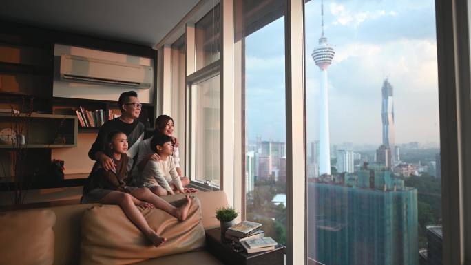 在吉隆坡，一个亚裔华人家庭带着两个孩子透过窗户观看美丽的日落