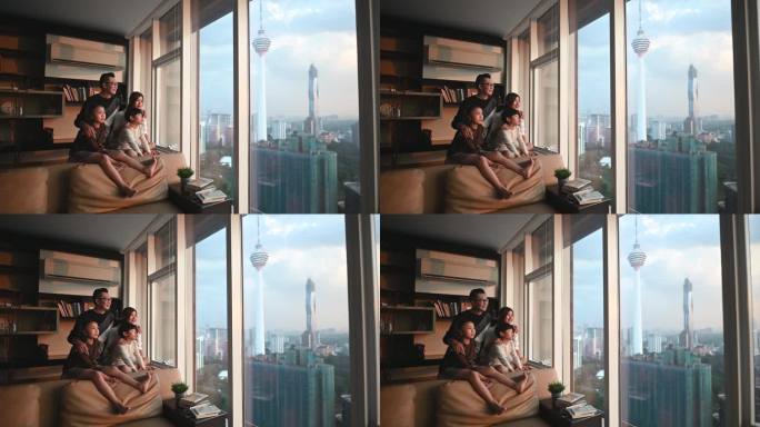 在吉隆坡，一个亚裔华人家庭带着两个孩子透过窗户观看美丽的日落