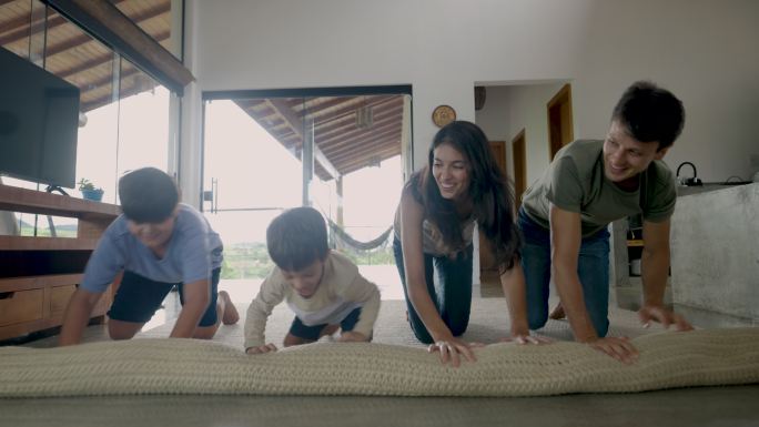 可爱的四口之家在家里展开地毯在地板上玩，开心地笑着