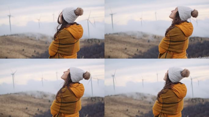 一位妇女在山顶上的风力涡轮机公园里，在云雾中欣赏日落。高度的观点。