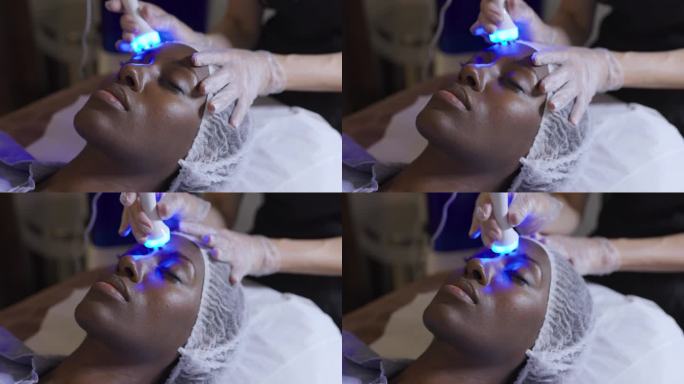 美丽的黑人年轻女子在水疗中心接受超声波和光疗面部护理