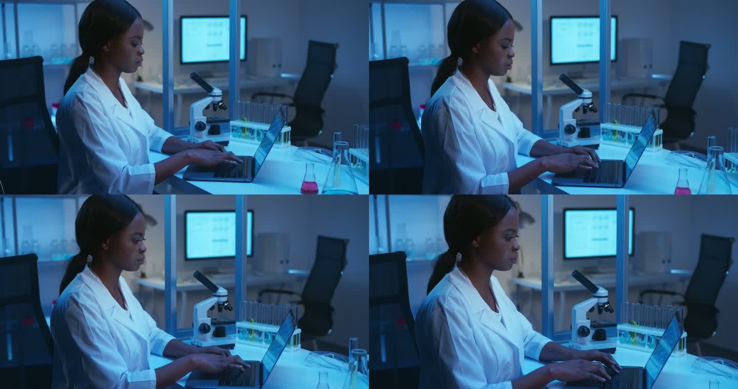 一位年轻漂亮的非洲裔美国科学家，穿着白色实验室外套，在一个现代化的实验室里用笔记本电脑工作