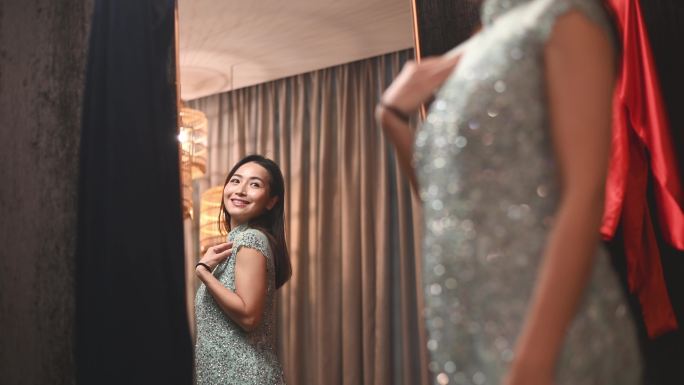 一名亚裔中国妇女穿着中国传统旗袍，看着镜子，在传统精品店微笑
