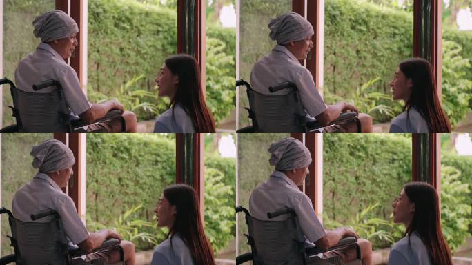 年轻的支持性亚洲女性看护者帮助患者闻到窗口的新鲜空气作为帮助之手，与癌症患者在轮椅上放松的亚洲老年人