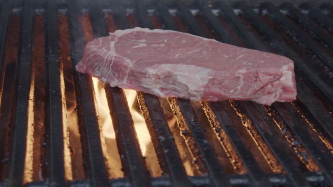 厚厚的生牛里脊肉慢动作地扔到烤架上，牛排击中时火焰燃烧