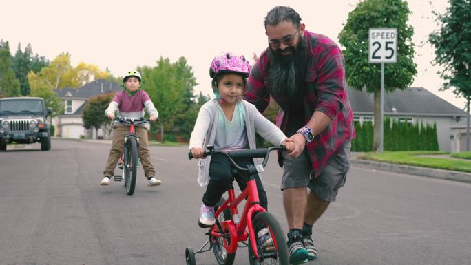 一位美国原住民父亲正在帮助他的小女儿学习骑自行车