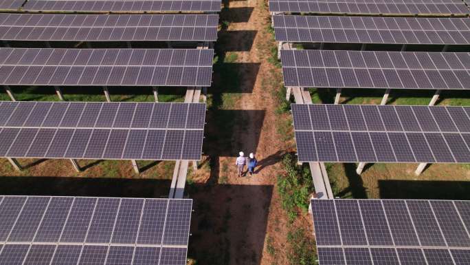 工程师和技术人员在太阳能电池板阴影下检查太阳能电池板农场的鸟瞰图