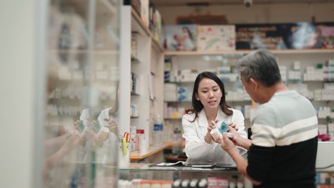 一名亚裔华裔高级男子在药店药房寻求女药剂师关于医疗用品的建议