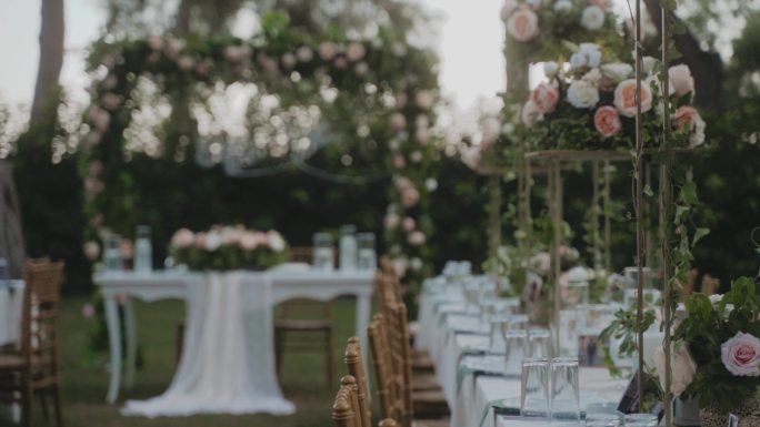 花园中令人惊叹的婚礼布置装饰，白色桌布和木制椅子的桌子。美丽的节日气氛。花园里到处都是粉红色和白色的