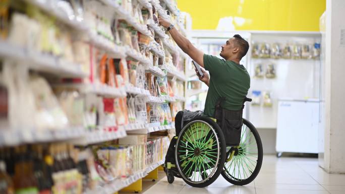 周末，一名残疾亚裔印度男子坐轮椅在超市购物，用他的智能手机查看购物清单
