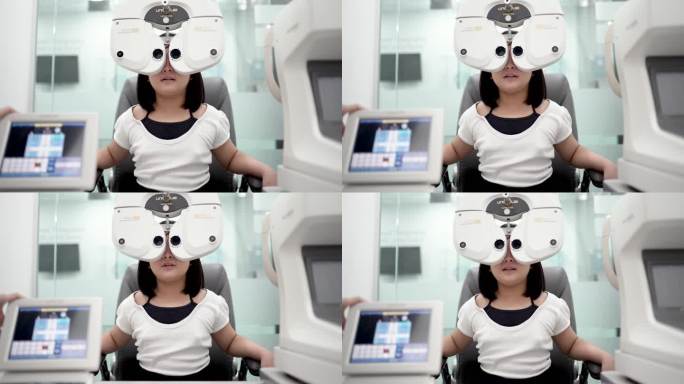 一个亚裔中国女孩坐在椅子上，在眼科诊所用数字验光仪做视力测试