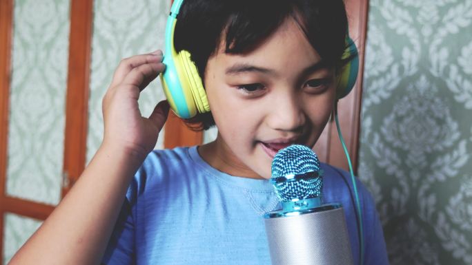 一个亚洲泰国男孩在客厅里用麦克风和耳机，穿着蓝色T恤唱卡拉OK的4K画面。这是一个简单的家庭乐趣的概