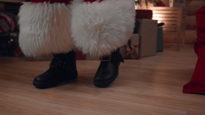圣诞老人脚穿靴子的特写镜头，在他满屋子礼物的木地板上行走