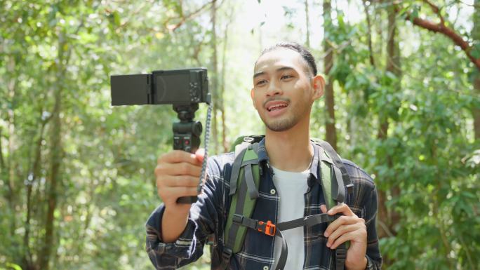 亚洲英俊男背包客vlogger独自在森林中旅行。吸引人的男子旅行者使用手机录制视频博客，在假期旅行中