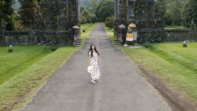 鸟瞰旅行者妇女在印度尼西亚巴厘岛印度教寺庙门口奔跑