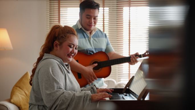 亚洲身材高大的年轻夫妇在家里一起玩钢琴和吉他音乐