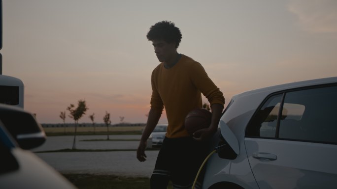 斯洛·莫，一个年轻的篮球运动员，黄昏时在停车场给他的电动车充电