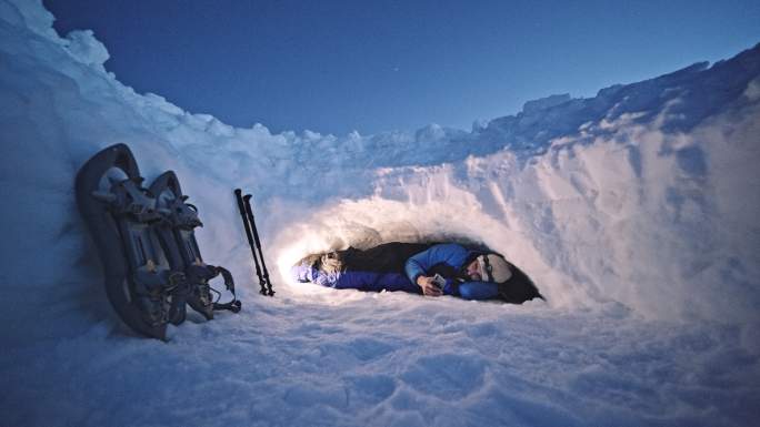 成熟的游客晚上在雪地里使用手机。在冬天的山上露营，独自在大自然中。