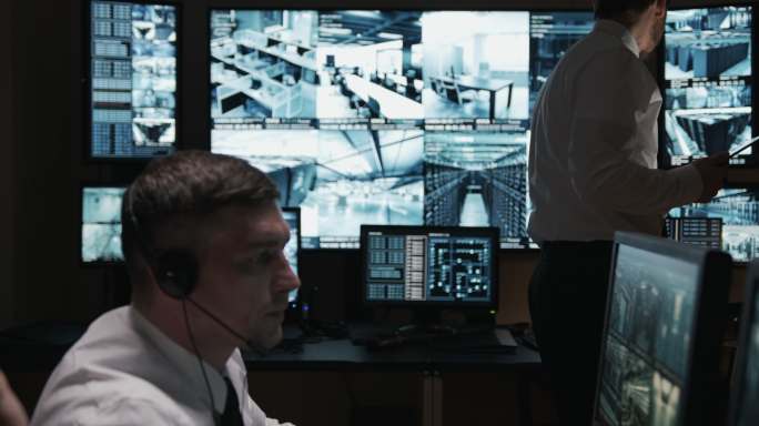两名保安全神贯注地在电脑前工作，第三名保安正在平板电脑上阅读新闻