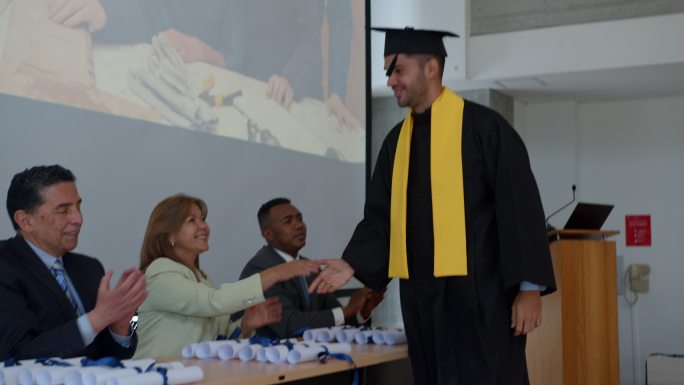 在毕业典礼上，骄傲的男学生收到毕业证书，与所有老师握手，然后举手看着同学