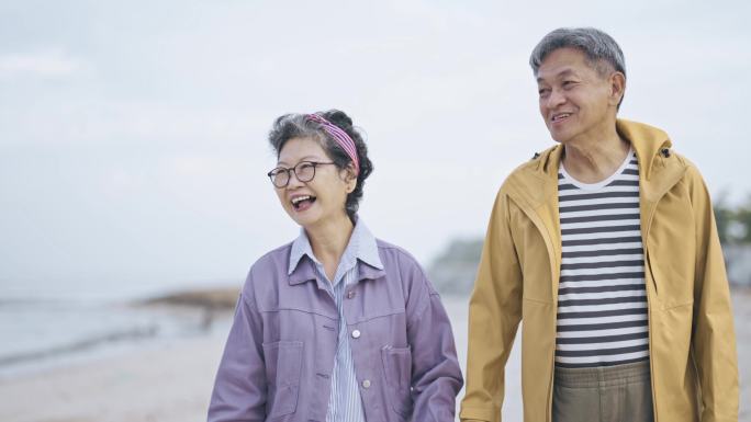 亚洲华人老年夫妇在海滩上穿着暖和的衣服看着别处