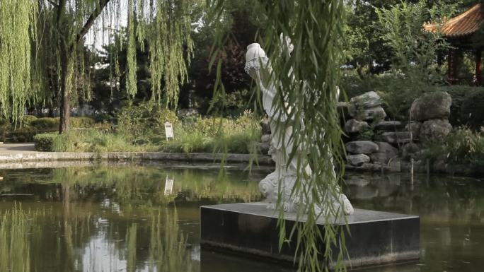 怡园公园湖中坐立一尊白色菩萨雕像掩映柳间