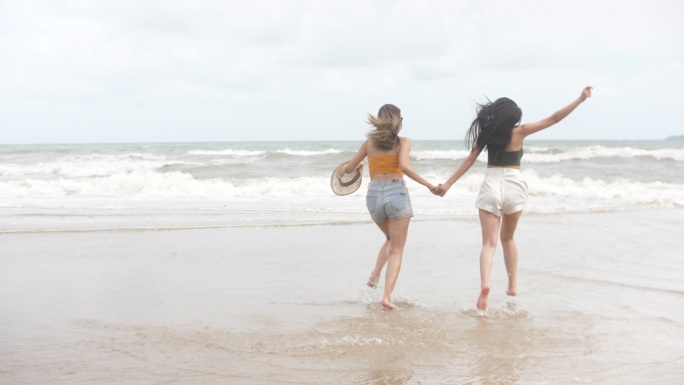 两个女人在海滩上享受和奔跑，手牵着手跑进大海