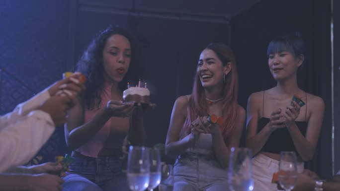 一群年轻时尚的人在晚上聚会，在生日蛋糕上吹蜡烛，同时使用五彩纸屑烟火