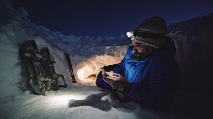 成熟的游客晚上在雪地里使用手机。在冬天的山上露营，独自在大自然中。