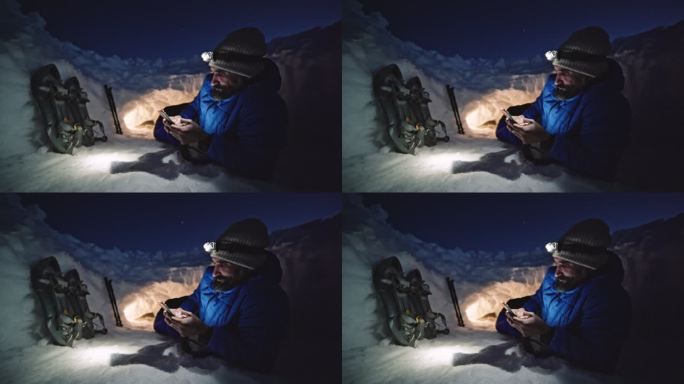 成熟的游客晚上在雪地里使用手机。在冬天的山上露营，独自在大自然中。