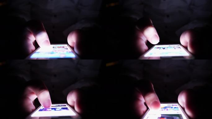 一个小男孩晚上在他的智能手机上玩——躲在毯子下面