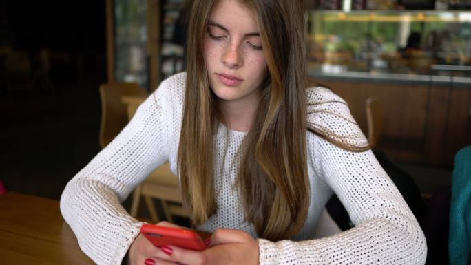 美丽的年轻女孩在咖啡馆发短信