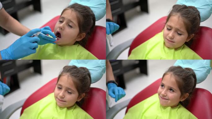 儿科牙医在牙根周围喷洒麻醉剂，而害怕但勇敢的女孩仍然坐在牙医的椅子上