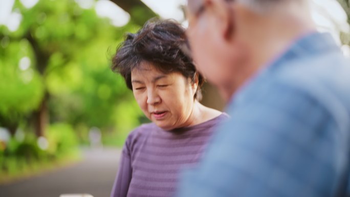 一对年长的夫妇坐在长凳上，在大自然中一起使用智能手机