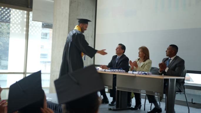 骄傲的男学生在毕业典礼上与老师和院长握手，同时领取毕业证书