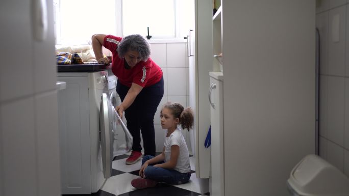 奶奶和孙女在洗衣房，把脏衣服放进洗衣机