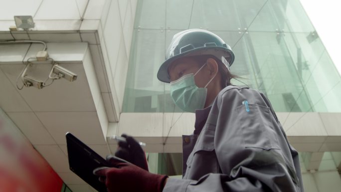 一名亚洲女技术员和一名检查员正在检查大楼外的安全摄像头。女触摸工程师