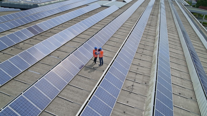 空中：两名电气工程师站在屋顶上一排光伏板中间交谈