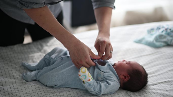 亚裔中国年轻父亲在床上为他的男婴扣扣子