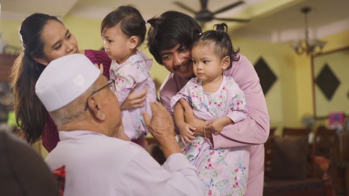 一个马来穆斯林孙子和他的家人穿着传统服装，在艾迪尔菲特里庆典上向他的祖父表示道歉。一个马来家庭在家里