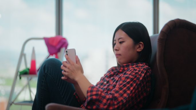 一个年轻的女人，从擦窗户休息，放松，在沙发上使用智能手机