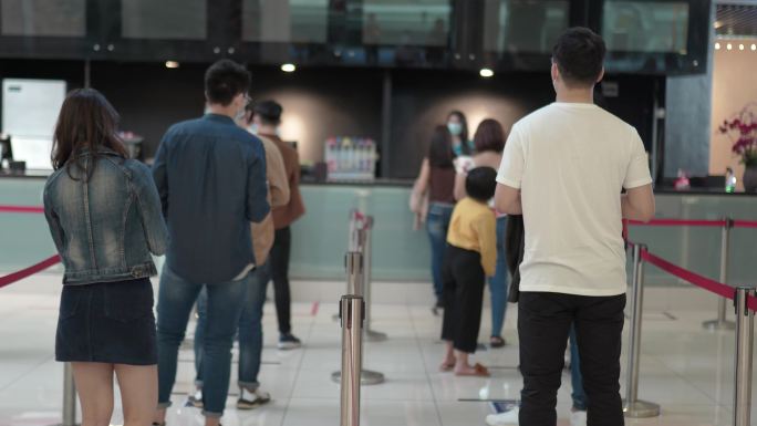 后视图：亚洲人群在电影院排队购买电影票和小吃，新的正常概念。社交距离。