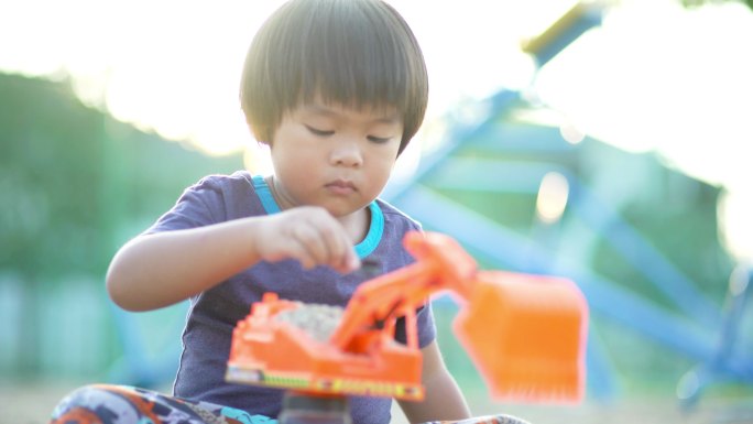 一个小男孩独自在操场上玩挖掘机玩具玩沙子