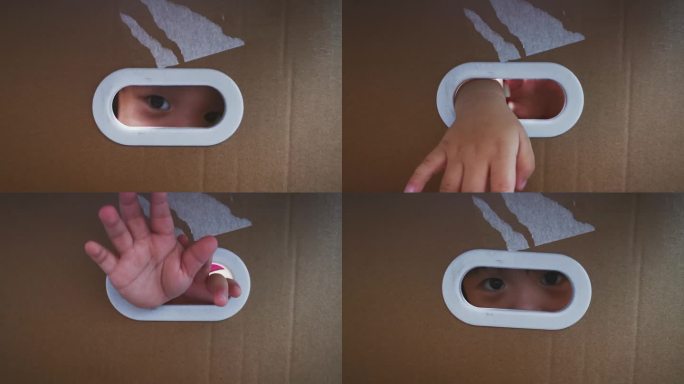 亚裔中国男婴从纸箱上的椭圆洞里偷看隐藏在纸箱里，用窗框阴影向外看