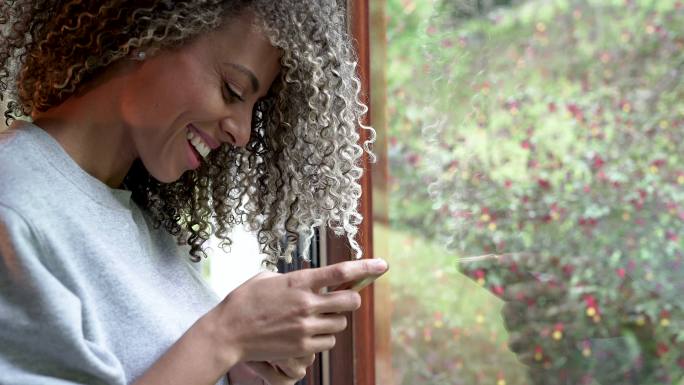 一个非洲头发的拉丁女人在她的客厅里用她的手机
