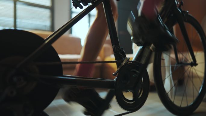 一个骑自行车的亚裔女子。她正在家里锻炼。通过在教练机上骑自行车和玩在线自行车游戏