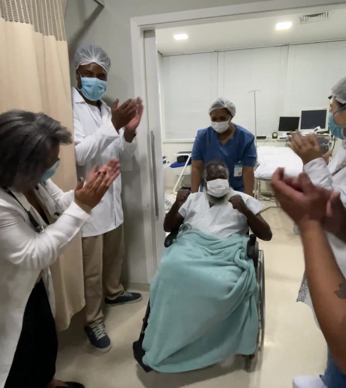 医生和护士们正在庆祝这位老人康复出院，戴着防护面罩，用移动设备拍摄