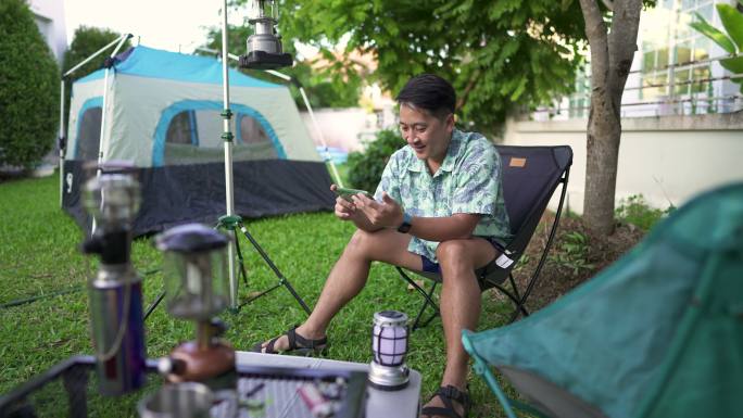 男人在后院露营时用手机看电视。