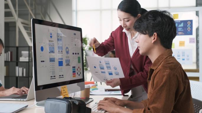 亚洲女性领导者反馈：移动应用程序设计线框原型，开发人员在现代办公室的台式电脑上