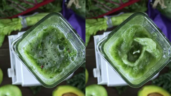 饮食概念：慢动作的直接下拍摄搅拌机混合蔬菜和水果排毒冰沙。厨房餐桌上的切菜板和搅拌机混合